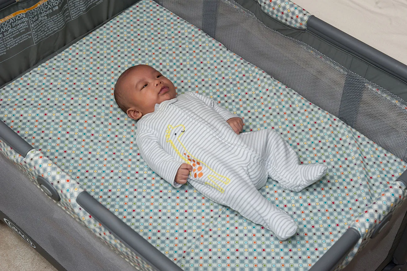 Newborn sleeping on their back in a crib with a single, fitted sheet.