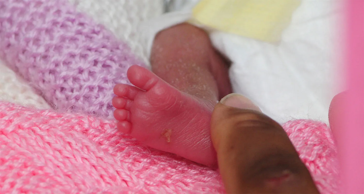An adult finger touching the bottom of a newborn baby’s foot as it rests on a blanket.