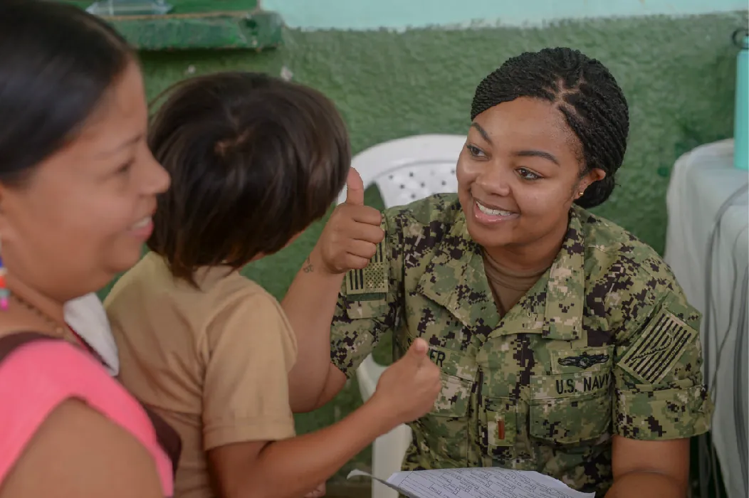 A soldier in uniform gives the thumbs up sign to a small child sitting in a parent's arms.