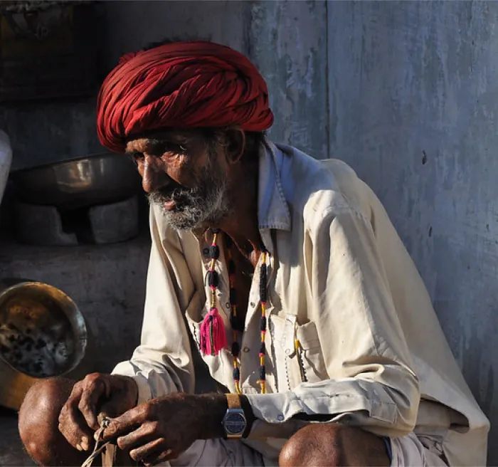 Photo of older individual sitting beside a stone wall.