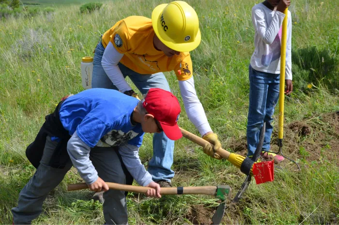 Photo of child and adult using an ax to dig the ground.