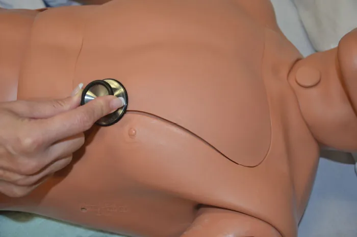 A photo of a hand assessing apical pulses using a stethoscope.