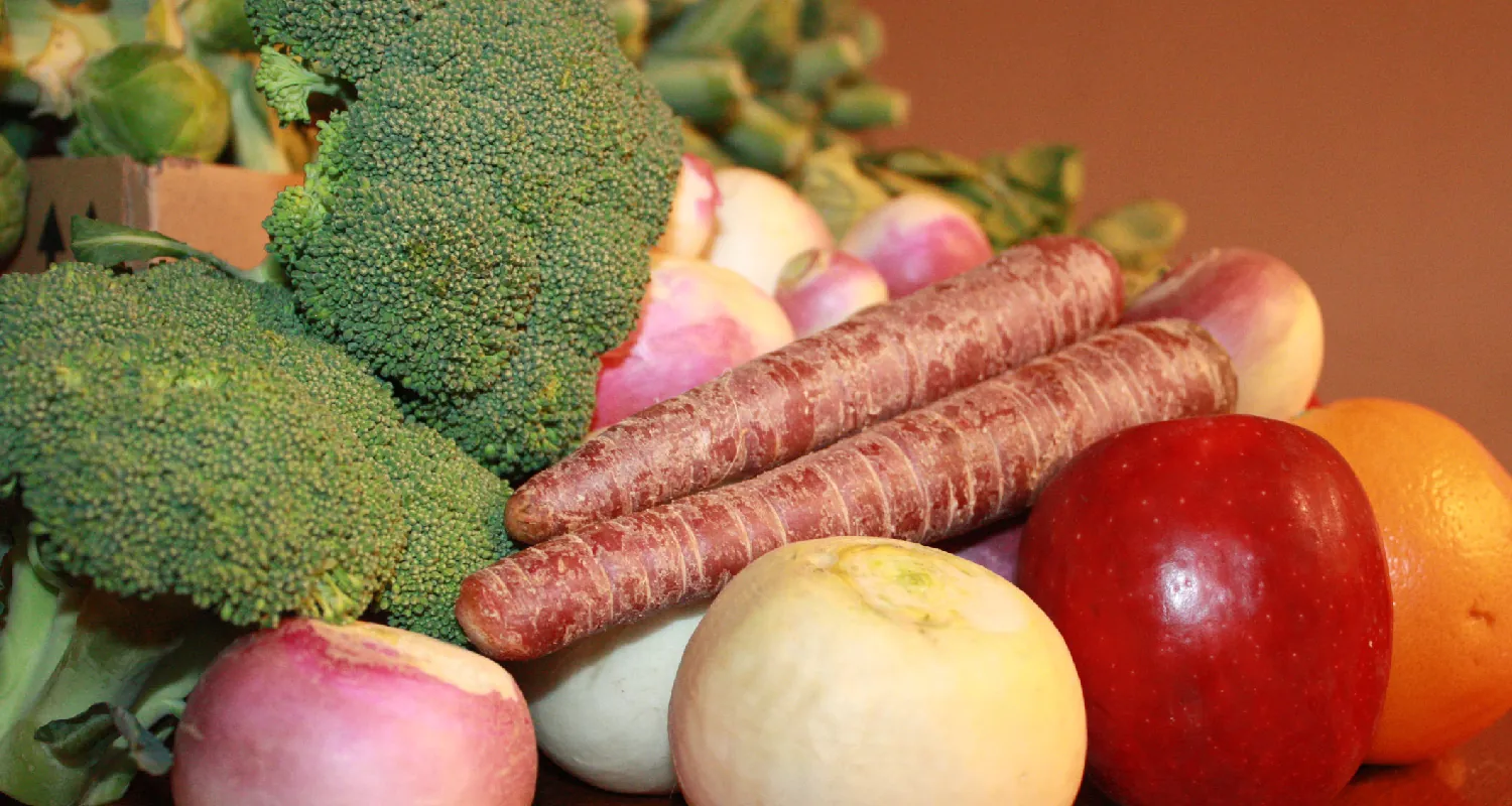 A display of different vegetables including broccoli, and carrots, an orange and apple.