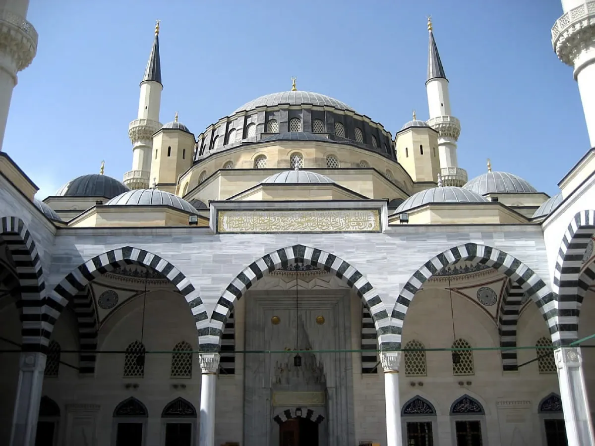 Photo of a Mosque with black and white archways, spires on either side of a rounded dome, and ornate windows and doorways.