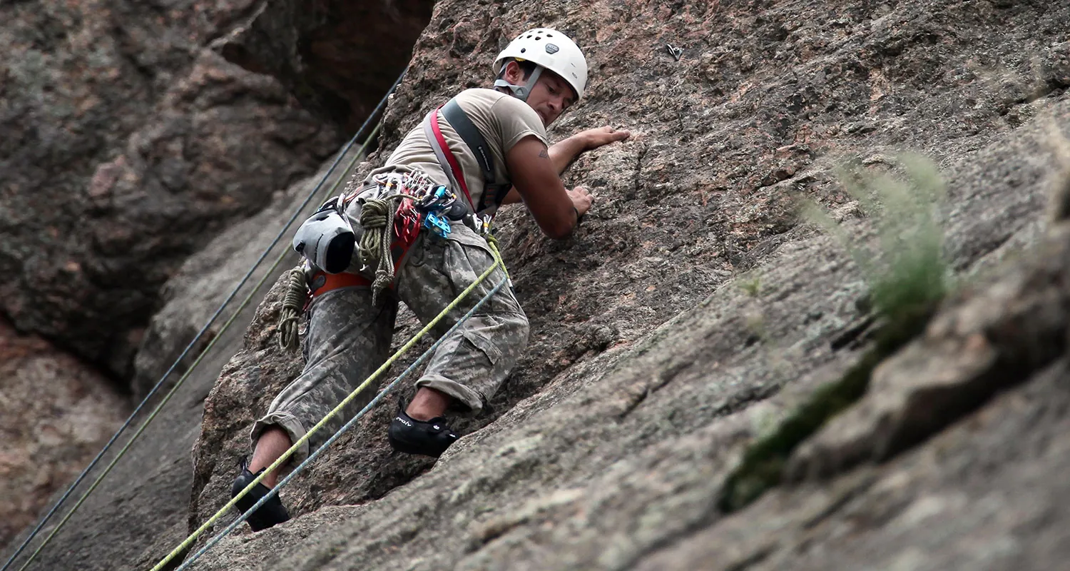 A rock climber climbing a rock with different colored ropes tied around.