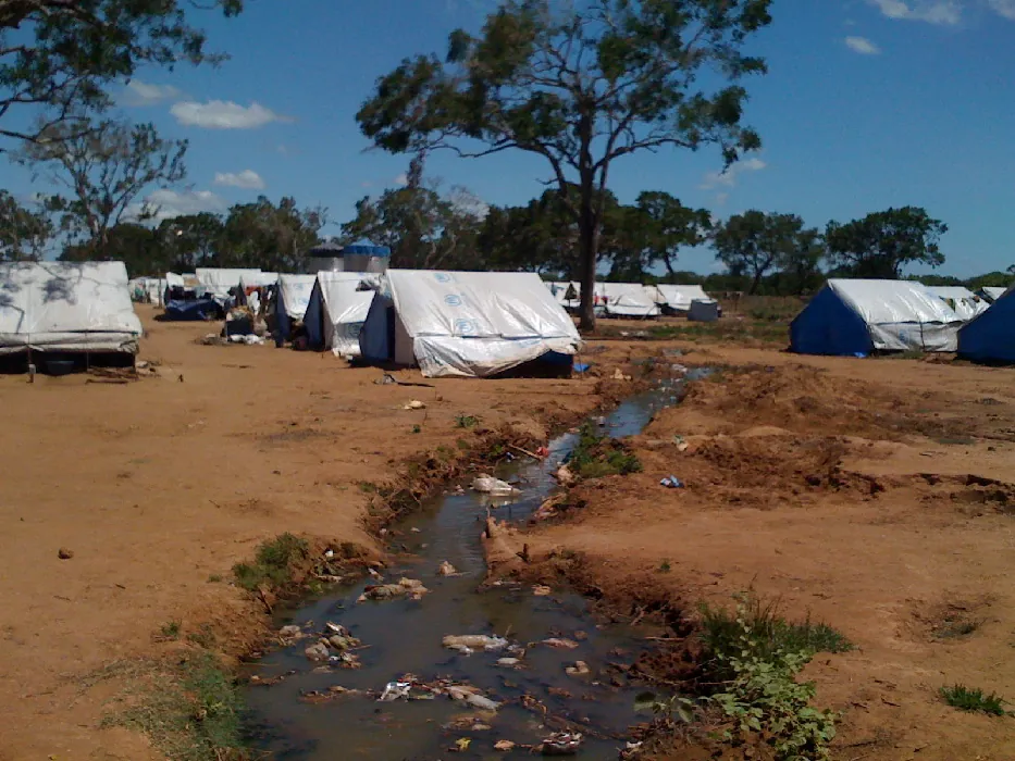 Rows of refugee tents are erected outside near a small stream.