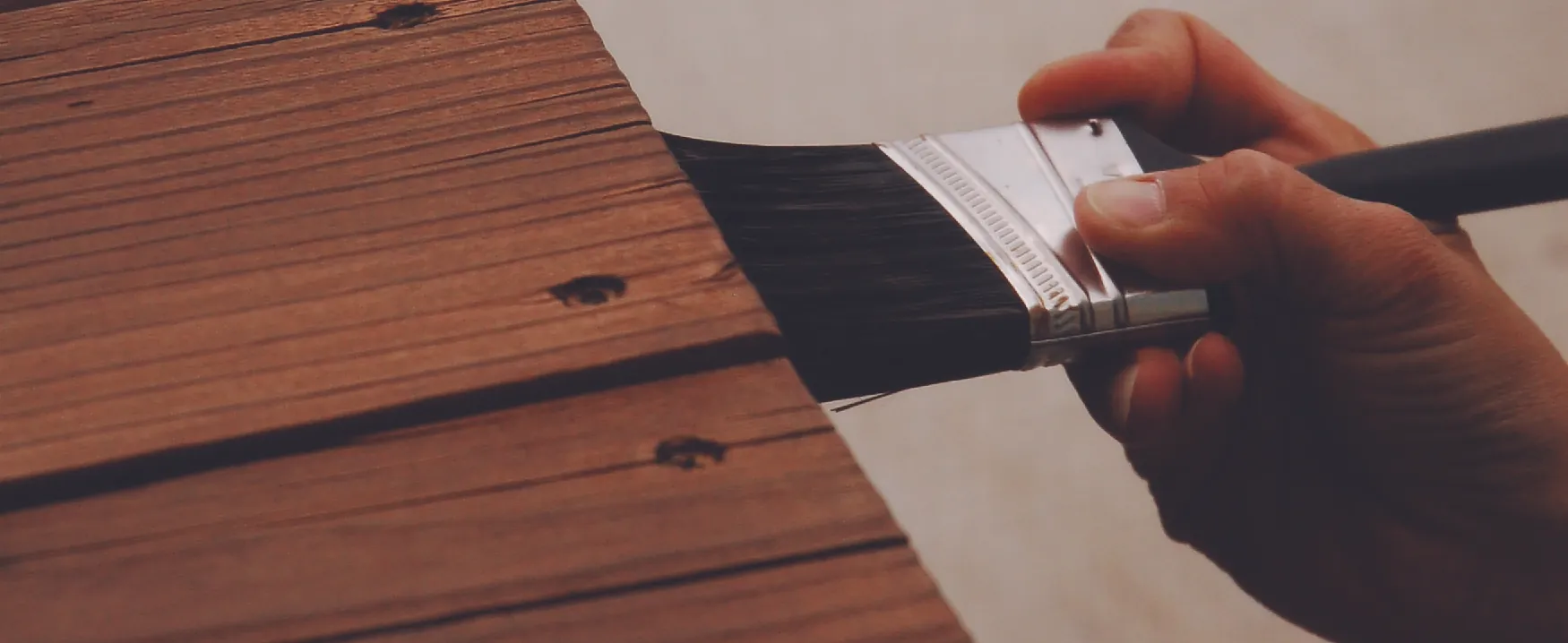 A photograph shows someone holding a brush applying stain to a piece of wood furniture.