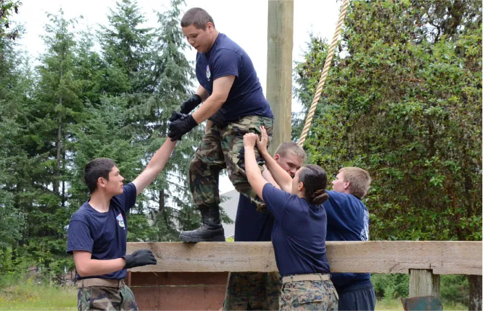 A group of individuals help a person over a wall.