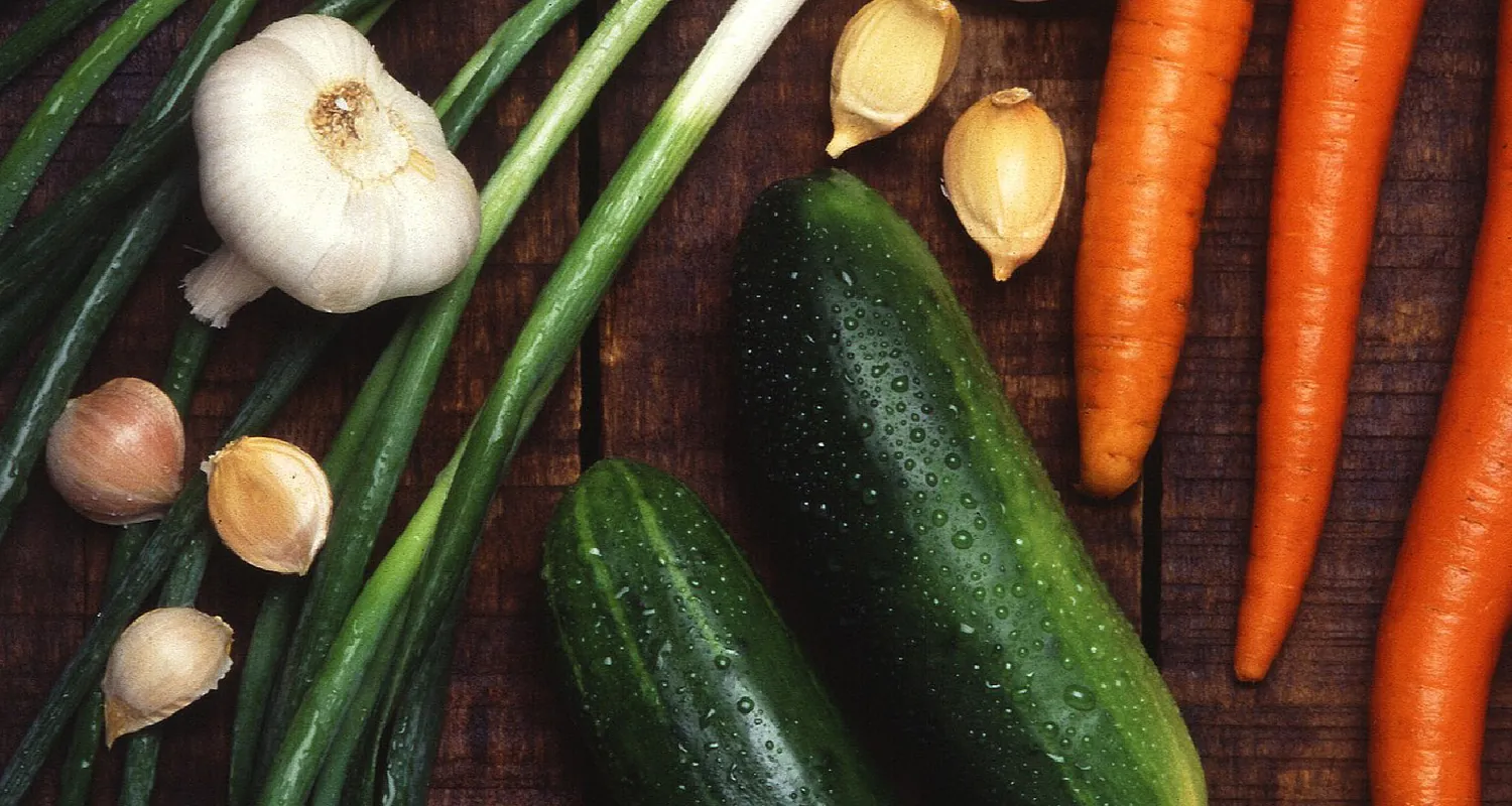 Garlic bulbs and cloves, cucumbers, and carrots arranged on a table.