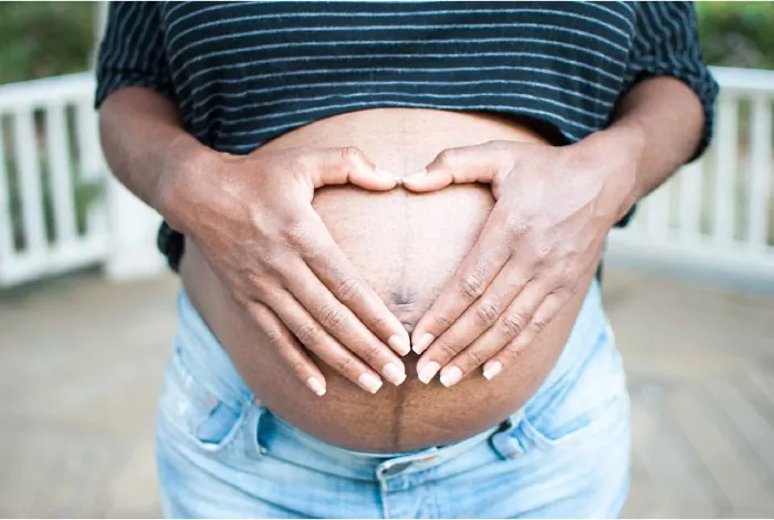 Photo of pregnant individual with their hands on their bare belly forming a heart with their fingers.