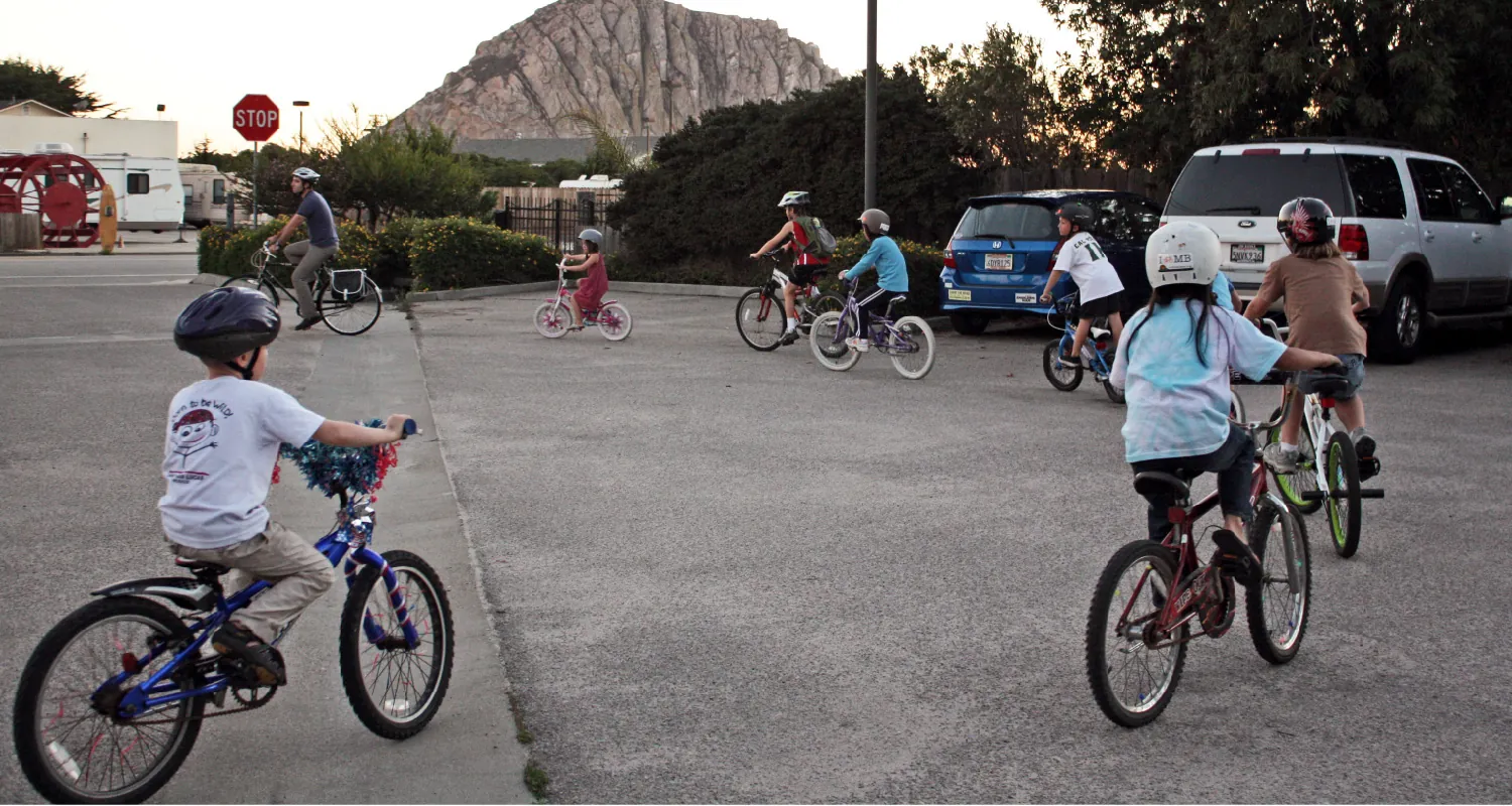 A group of adults and children ride bicycles in a parking lot.