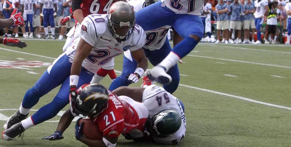 A photograph shows a football game with four football players trying to tackle a fifth player. A crowd is shown in the background.