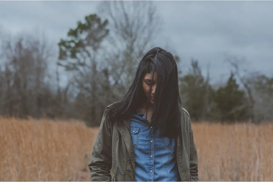 Photo of individual with long hair looking down. standing in a field.