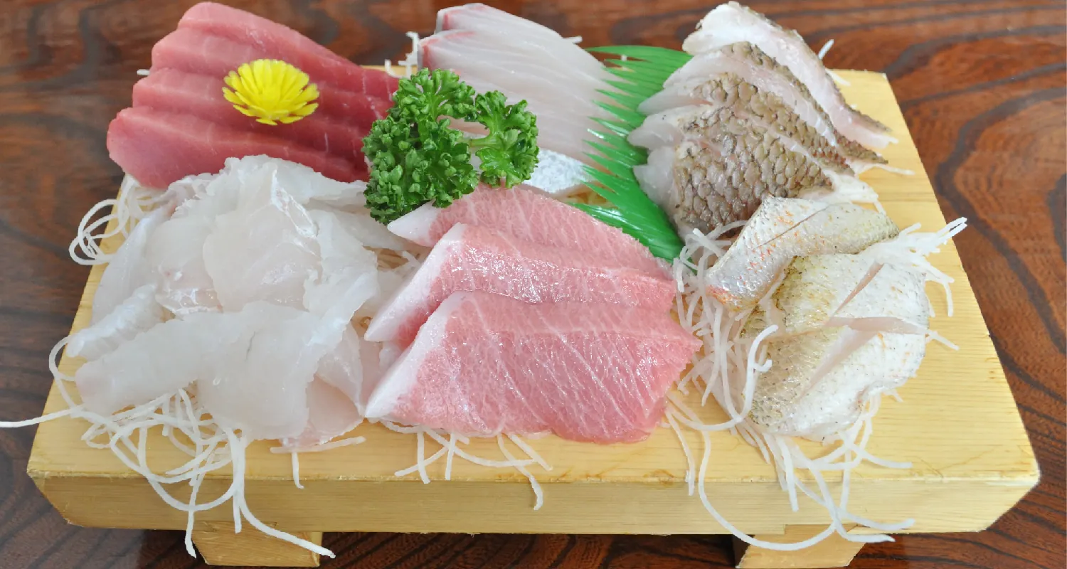 Six different types of raw fish are arranged on a small wooden board sat on a table.
