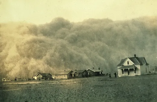 A photograph shows a group of houses on the Great Plains. A massive dust cloud fills the sky overhead.