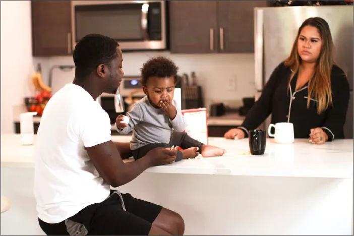 Photo of two individuals and a baby eating at a table.