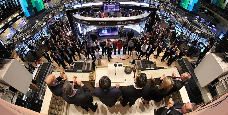 A group of stock traders watch a group of individuals ring the closing bell at the New York Stock Exchange.