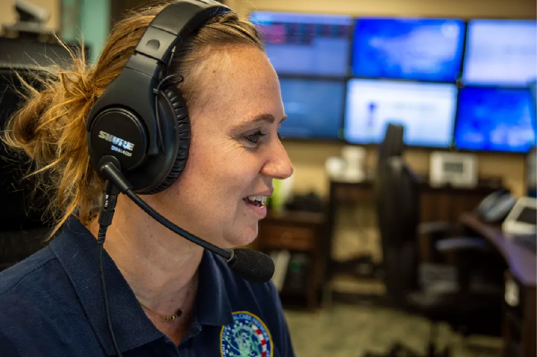 A nurse sits at a desk in an office wearing a headset with a microphone.