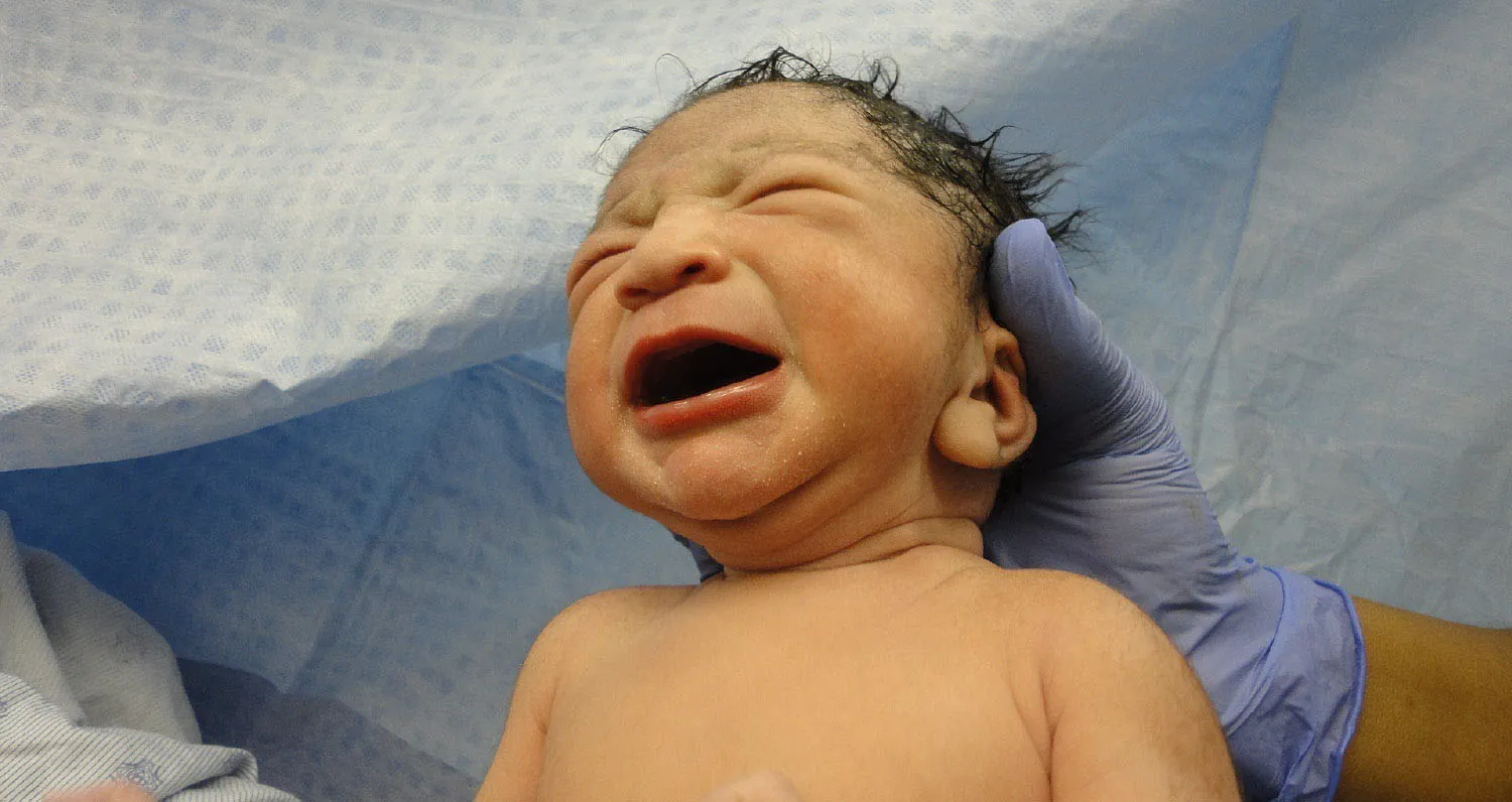 Photo of newborn child being held by a gloved hand in medical setting.