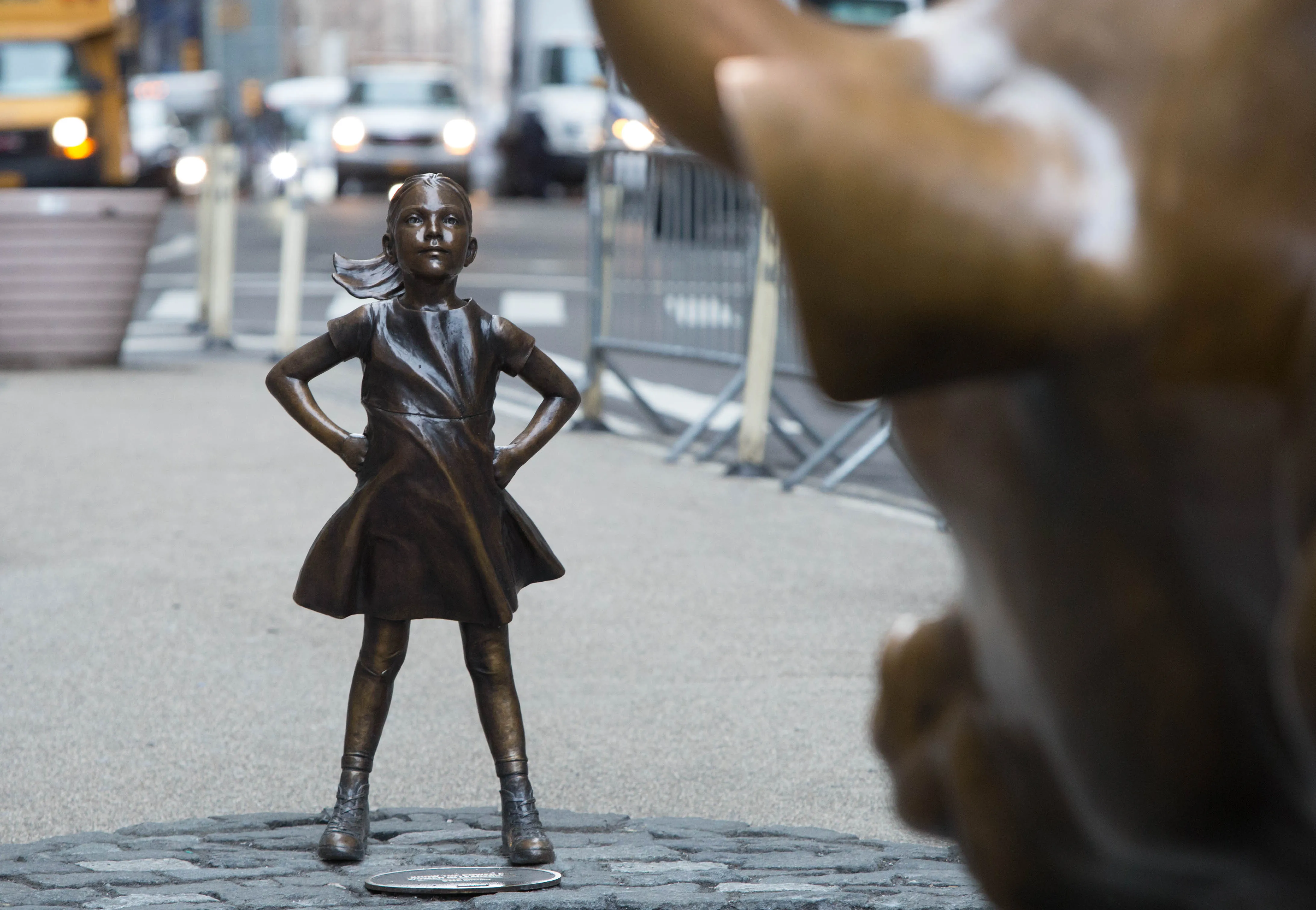 Bronze 'Fearless Girl' statue faces off against the Charging Bull, representing resilience and female empowerment in a dynamic urban setting.
