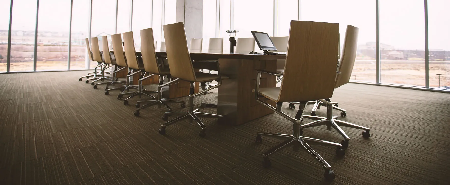A sleek, empty conference room with a long wooden table, modern chairs, and expansive windows offering a clear view of the sparse outdoor landscape, awaiting its next meeting.