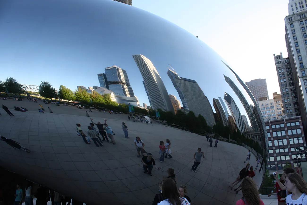 A photo shows the large, extremely smooth and reflective bean shaped sculpture. The city skyline reflects in the bean's surface.