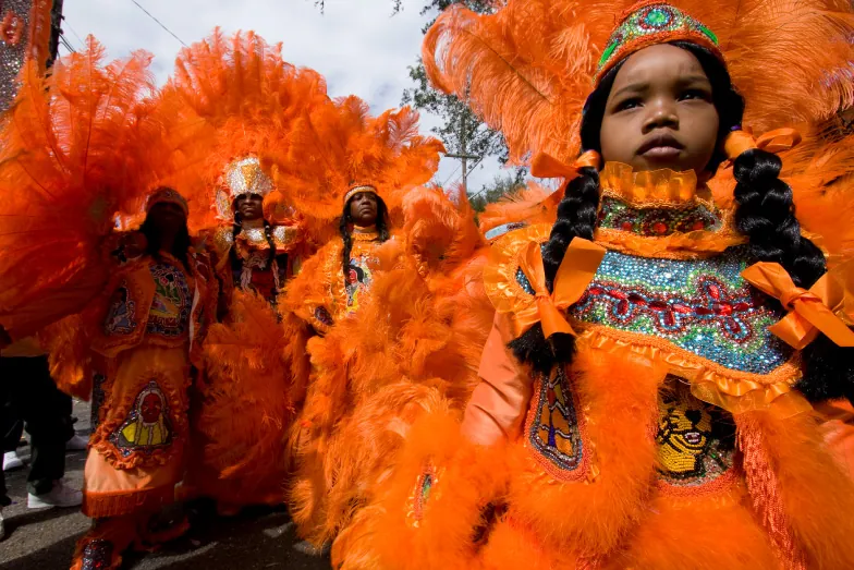 A groups of Louisiana Mardi Gras Indians dressed in bright orange feathered Mardi Gras Indian outfits.