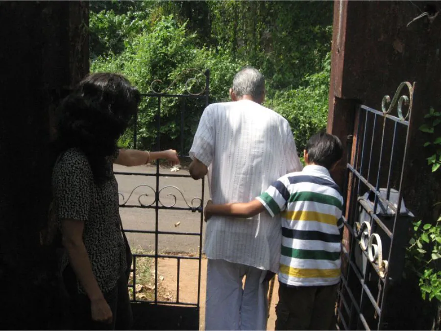 Photo of young child assisting older individual in walking through a garden gate while another individual looks on.