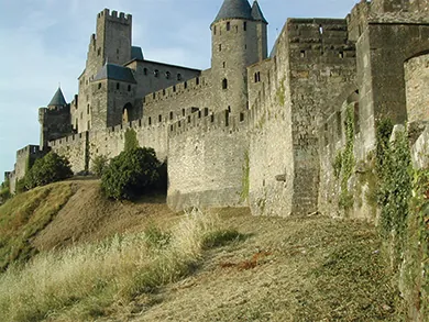 A photograph shows the medieval walled city of Carcassonne. It is surrounded by a high double wall with slots at the top, likely for archers or other defenders to use, and it incorporates several round parapets with narrow window openings.