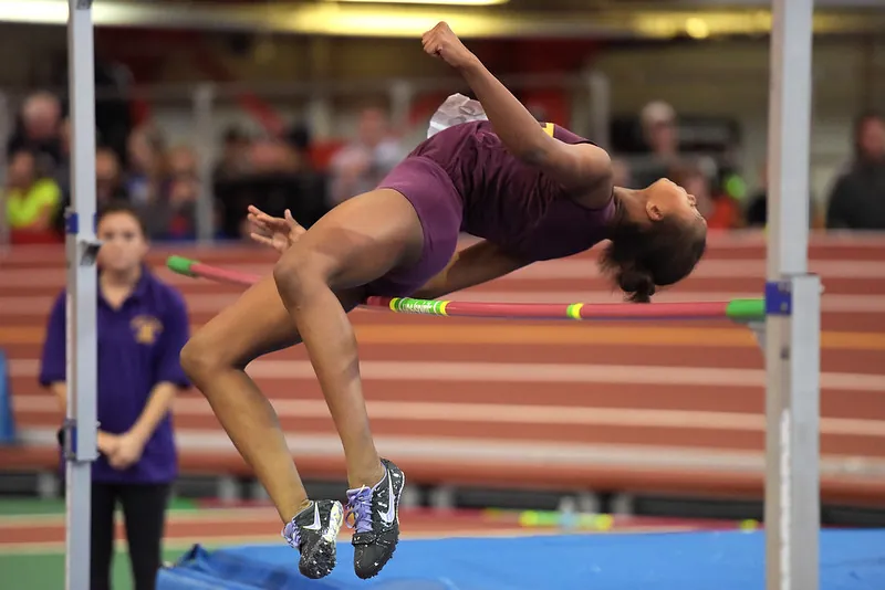 Illustration shows a woman, upside-down with an arched back, going over a pole vault.