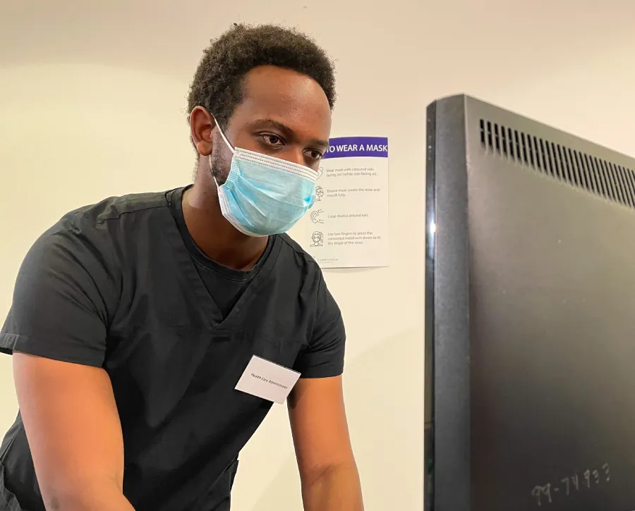 A color photograph of a nurse reviewing a patient's medical record on a portable computer stand in a hospital hallway.