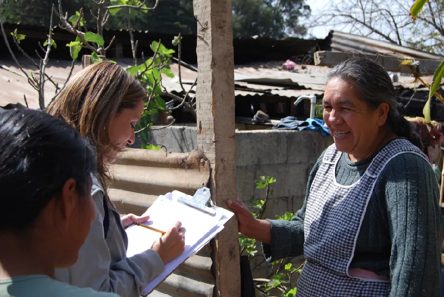 A person writes on a clipboard while talking to two other people.