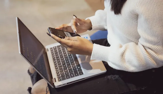 A photo shows a person using a phone and laptop computer.
