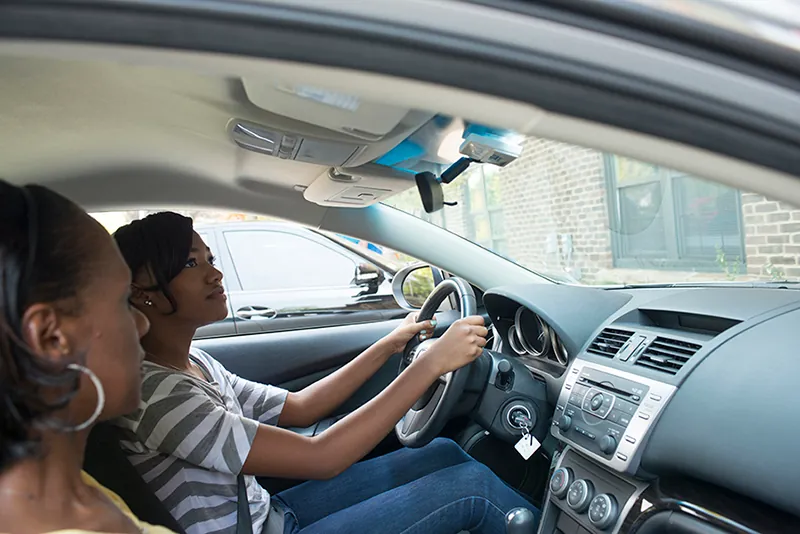 Two people are in a car, one is a passenger and the other is driving the vehicle.