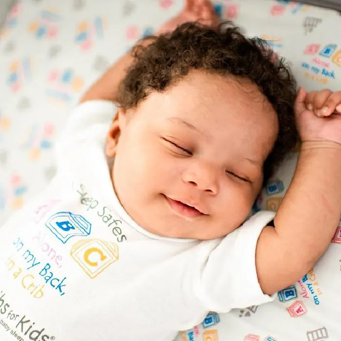 Photo of baby sleeping with their arms above their head and smiling.