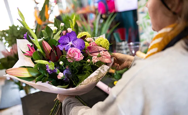 Photo shows a person arranging a floral bouquet.