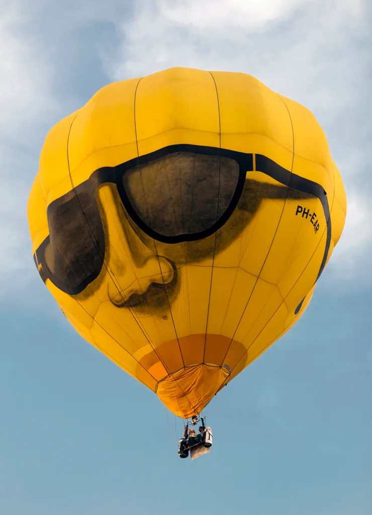 Floating high with style! A vibrant yellow hot air balloon, adorned with a cool face and sunglasses, glides across the sky.
