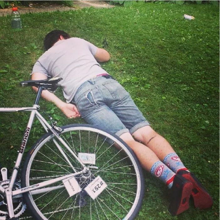 Photo of individual napping on the grass, face down, next to a bicycle.
