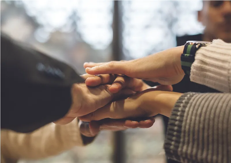 Photo of different people putting their hands together in the center, mimicking a sport’s cheer.