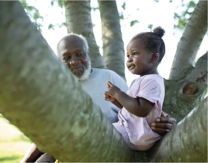 Photo of child sitting on a tree limb being supported by an older individual.