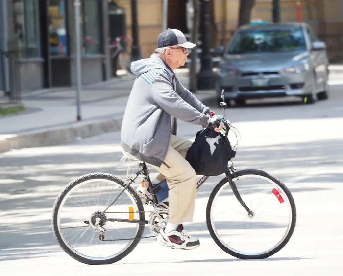 An older adult is riding a bicycle across a street.