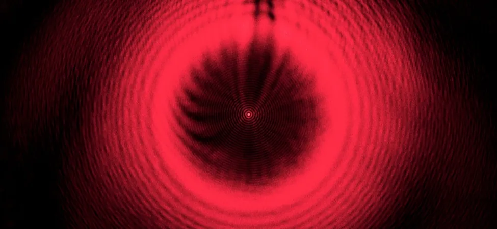 Figure shows a series of red concentric rings on a black background. At the center is a bright red spot.