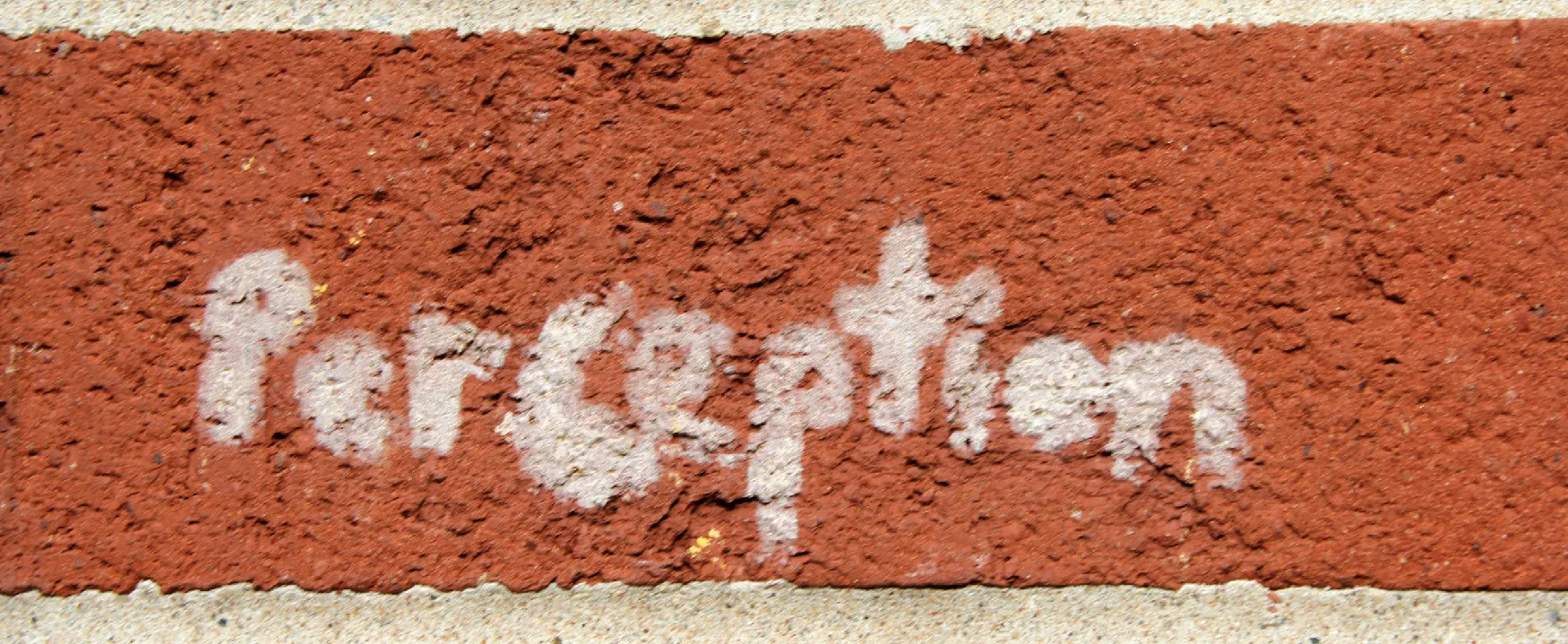The word 'Perception' is stenciled in white on a rough, textured red brick. The contrasting white text stands out against the brick's deep red hue and rugged surface.