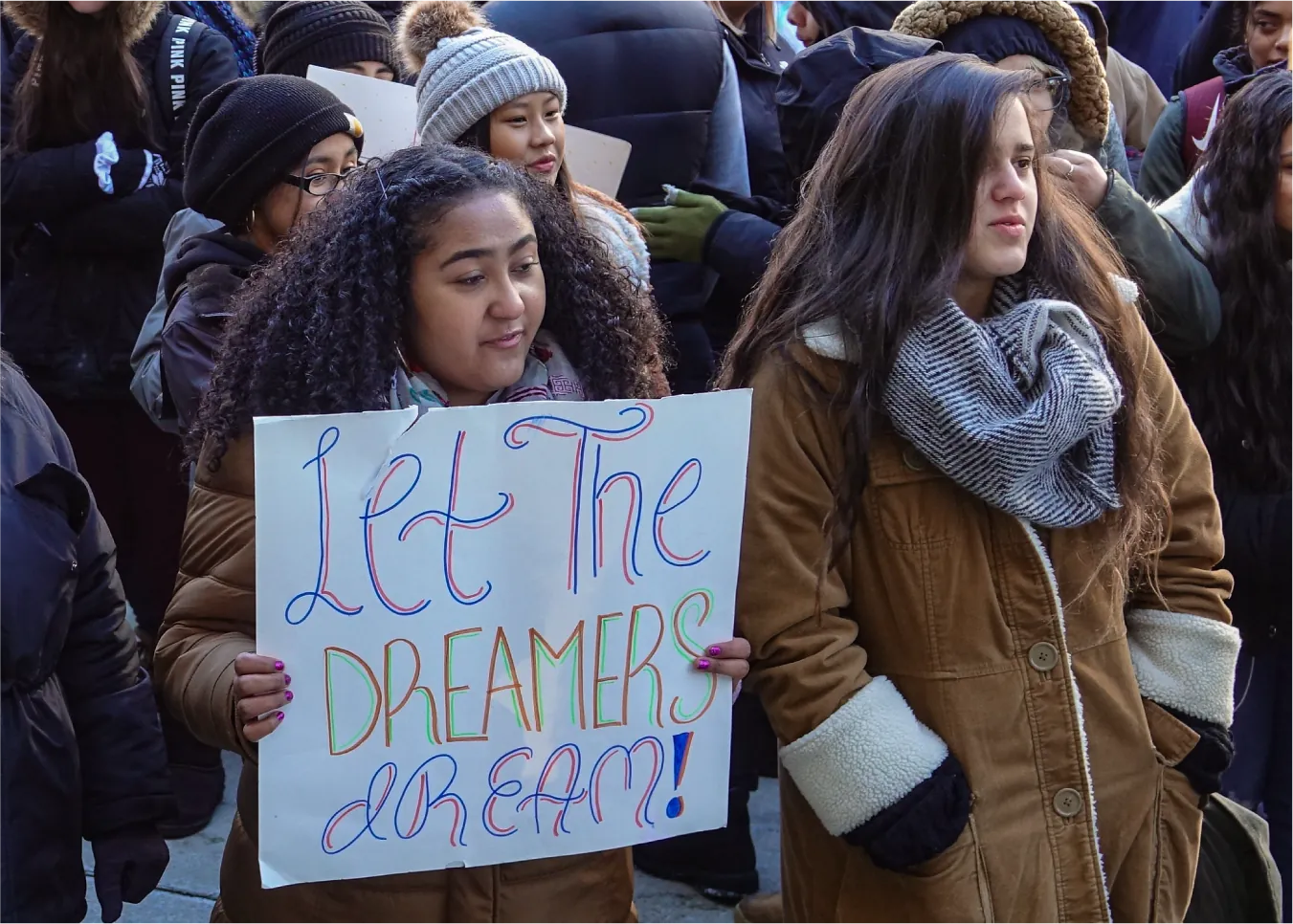 Photo of an individual holding a sign labeled “Let the dreamers dream!” among a group of people.