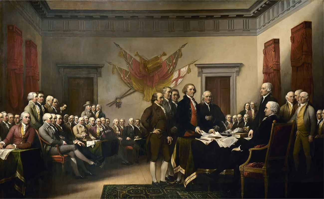 A painting shows members of the committee that drafted the Declaration of Independence presenting their work to the Continental Congress. Five men, including John Adams, Thomas Jefferson, and Benjamin Franklin, stand in front of a table at which other men are seated or standing. Jefferson is placing papers on the table. The room is filled with seated men, apparently the rest of the Continental Congress. British flags are mounted on the wall behind them.