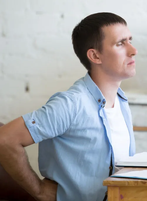 A color photograph shows a man sitting at a desk holding his lower back.