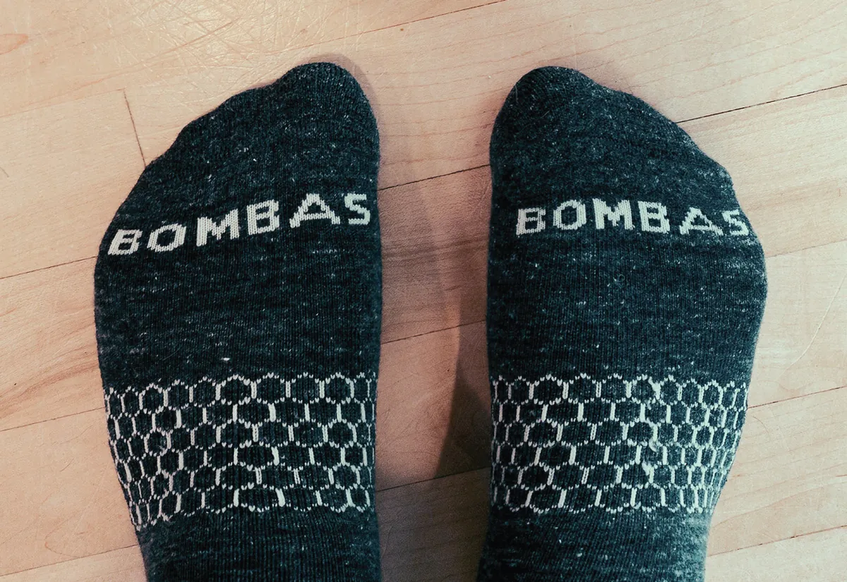 A pair of dark grey Bombas socks featuring a white honeycomb pattern, worn on a light wooden floor.