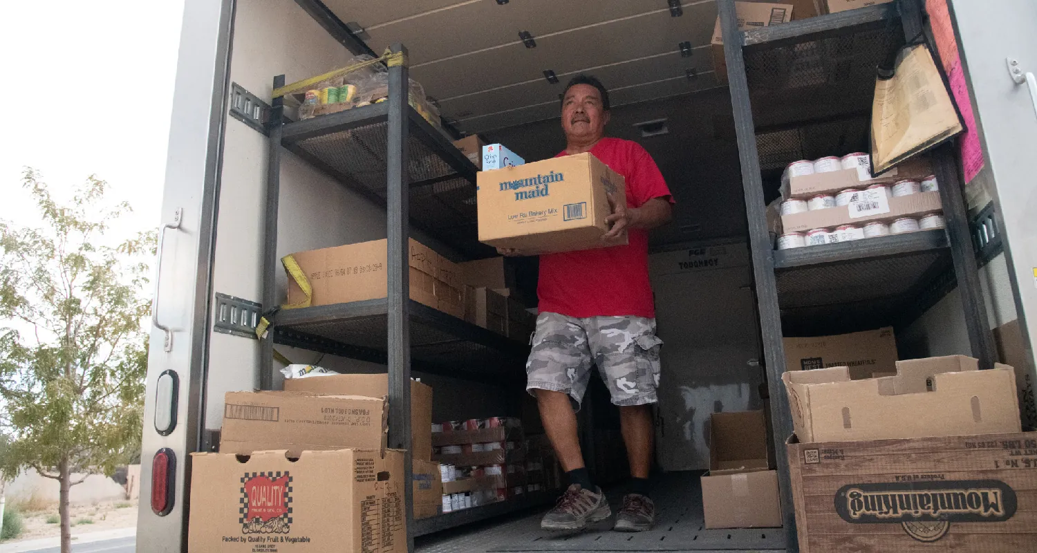 A worker carrying a box walks out of the back of a cargo truck filled with food in boxes.