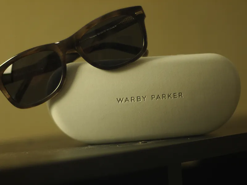 A pair of Warby Parker sunglasses are positioned on top of the sunglass case.