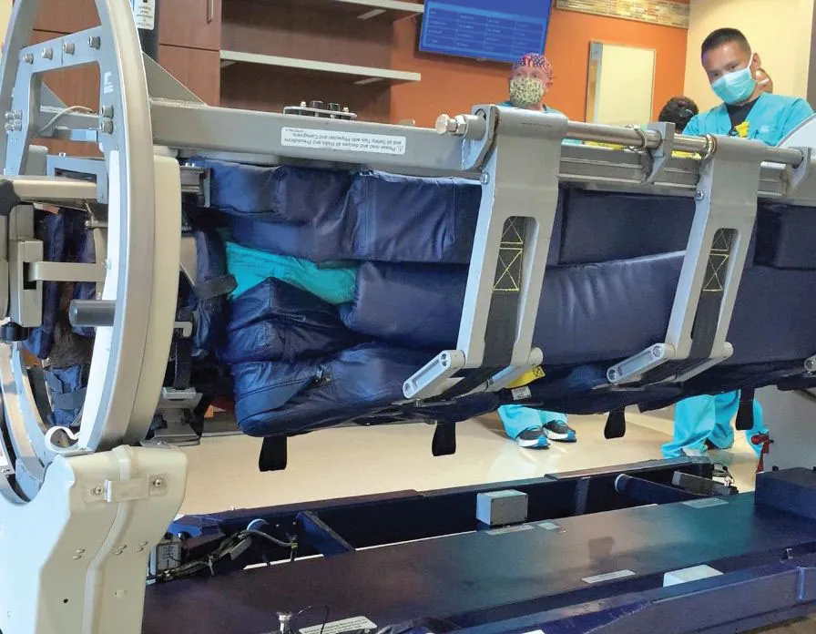 A color photograph showing a padded proning bed. The bed sits on device that allows it to turn to rotate the patient. There are large blue pads on the bed.